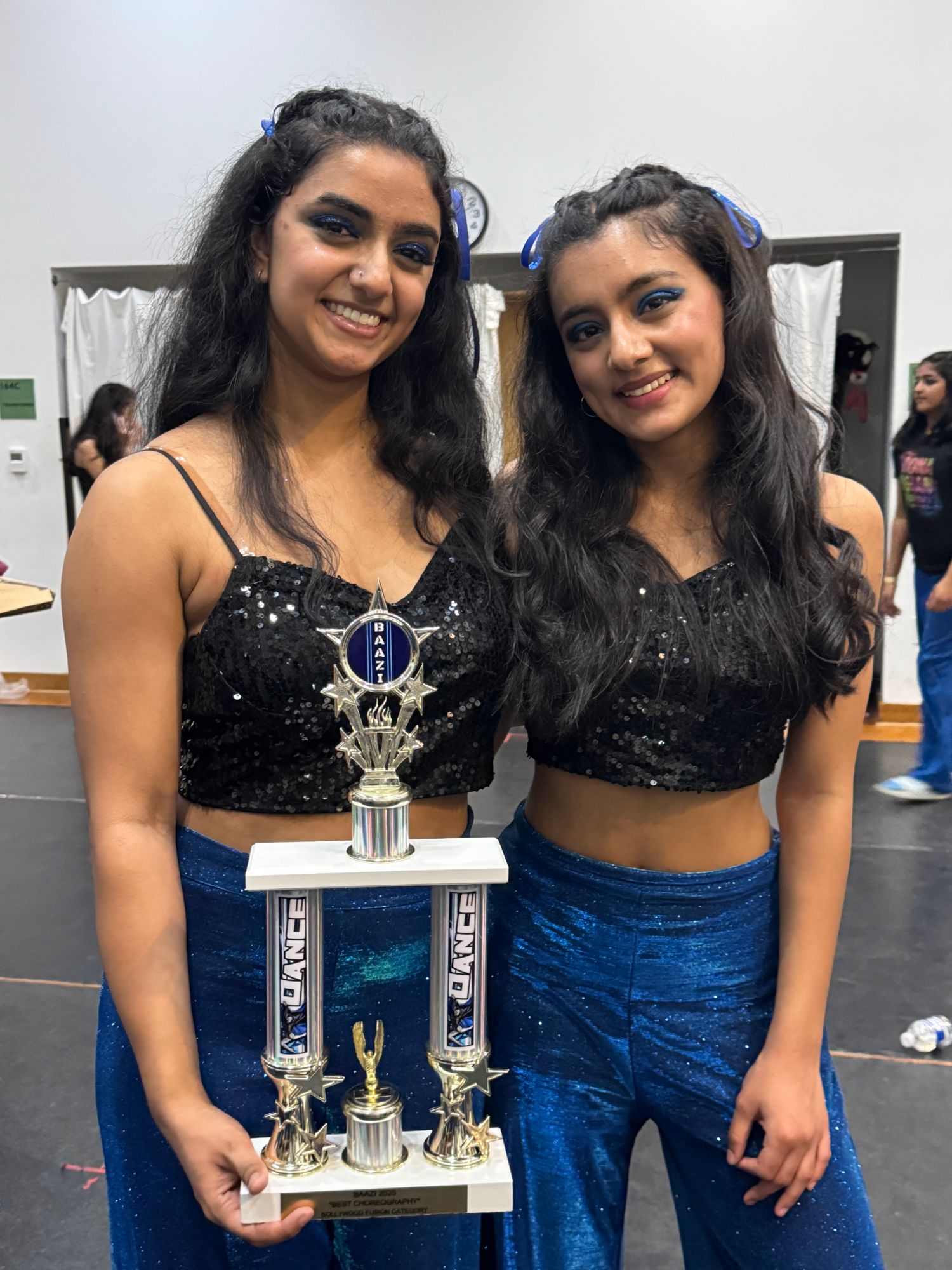 Neti and her team captain in sequined black tops and blue pants holding the Baazi Best Choreography trophy