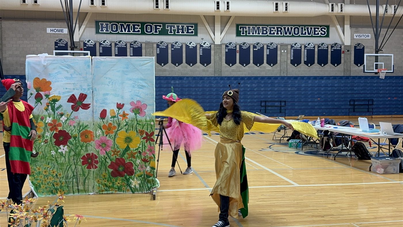 Neti with her yellow butterfly wings spread in front of a painted flower backdrop
