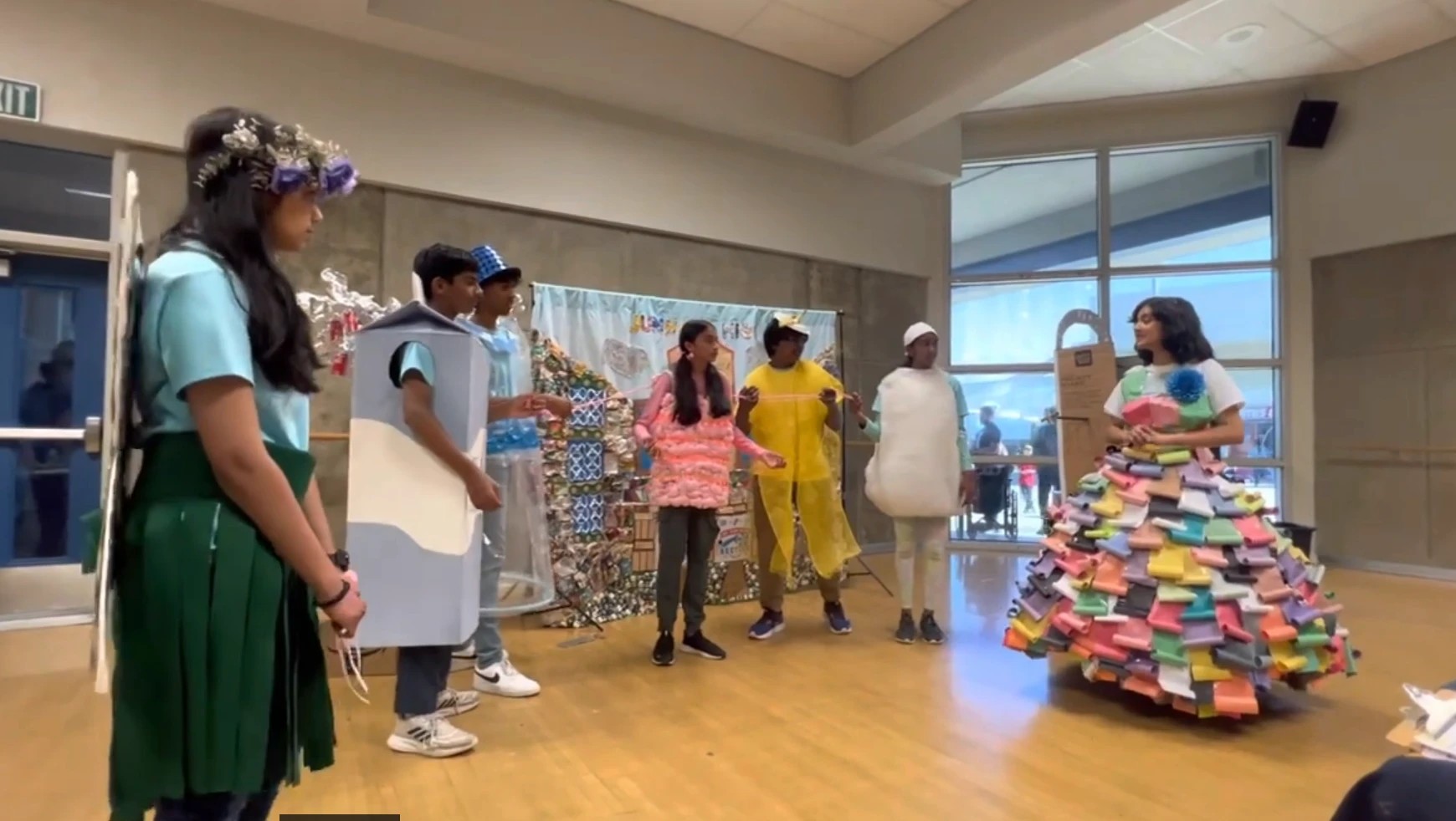 Neti in a hand-built dress of rolled colored paper beside teammates in handmade costumes, including a pink bubblegum costume