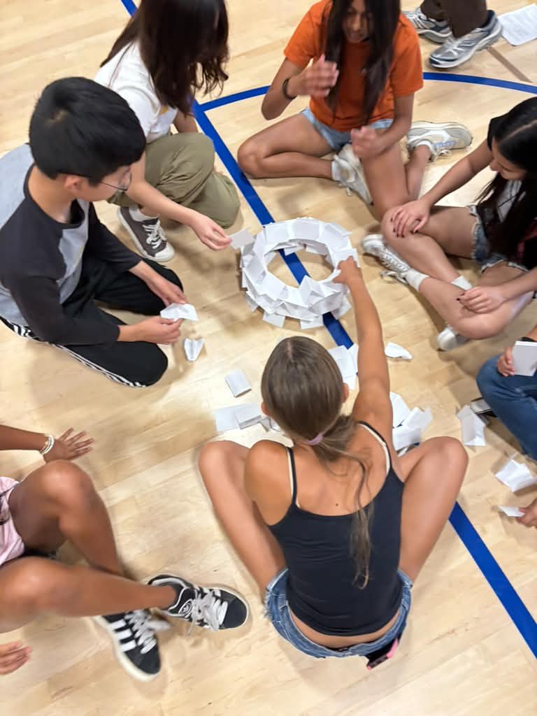 Teens on a gym floor building a ring out of paper cards