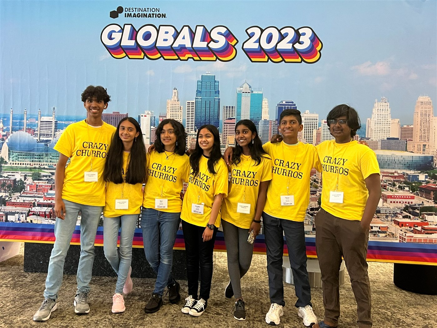 Seven DI teammates in yellow Crazy Churros shirts in front of a Globals 2023 Kansas City backdrop