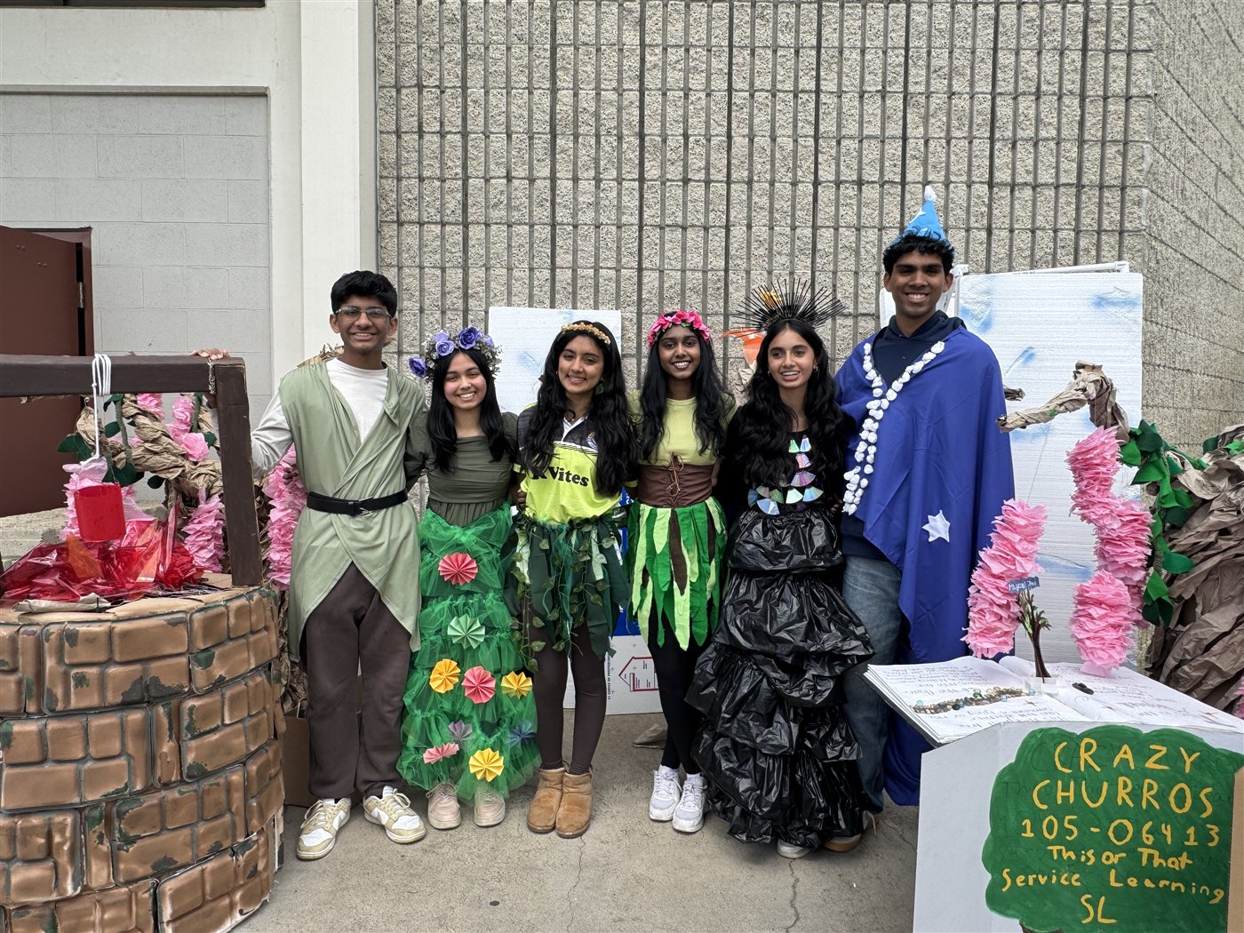 The 2025 DI team in handmade costumes next to a Crazy Churros sign
