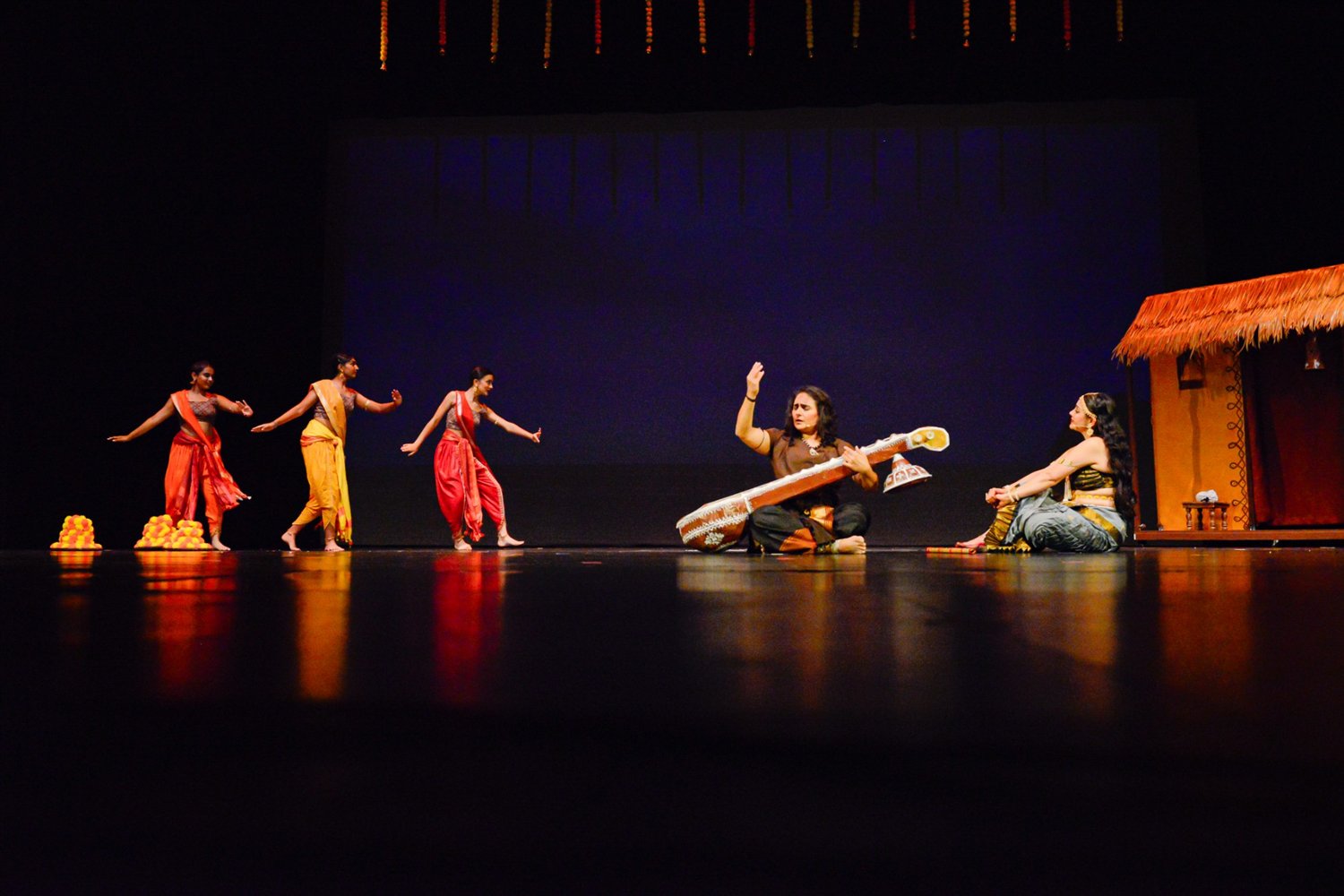 A scene from Vasantsena with a musician playing a large sitar and dancers behind