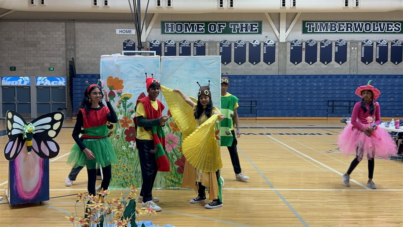 Neti in yellow butterfly wings on stage with teammates in bug costumes